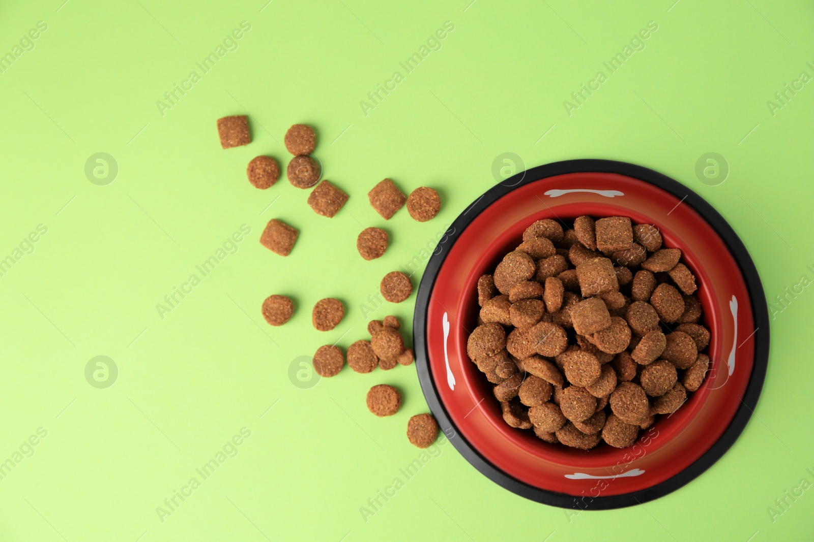 Photo of Dry dog food and feeding bowl on light green background, flat lay. Space for text