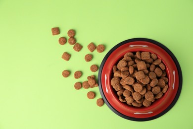 Dry dog food and feeding bowl on light green background, flat lay. Space for text