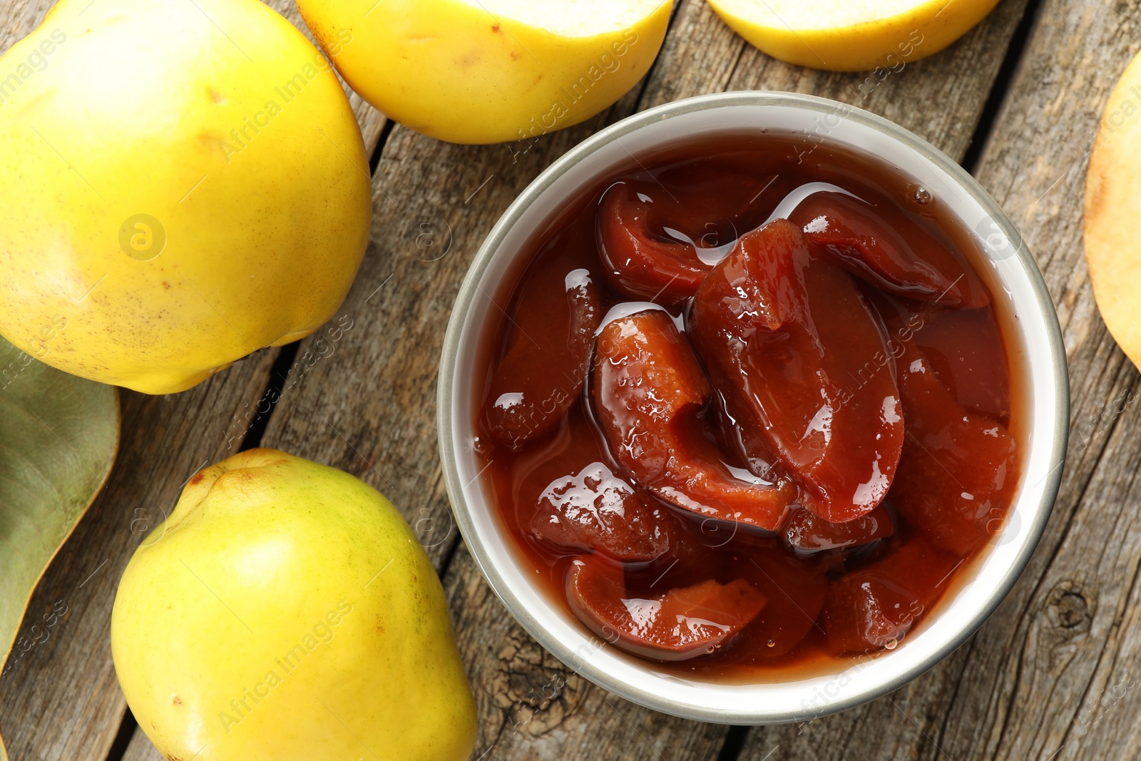 Photo of Tasty homemade quince jam in bowl and fruits on wooden table, flat lay