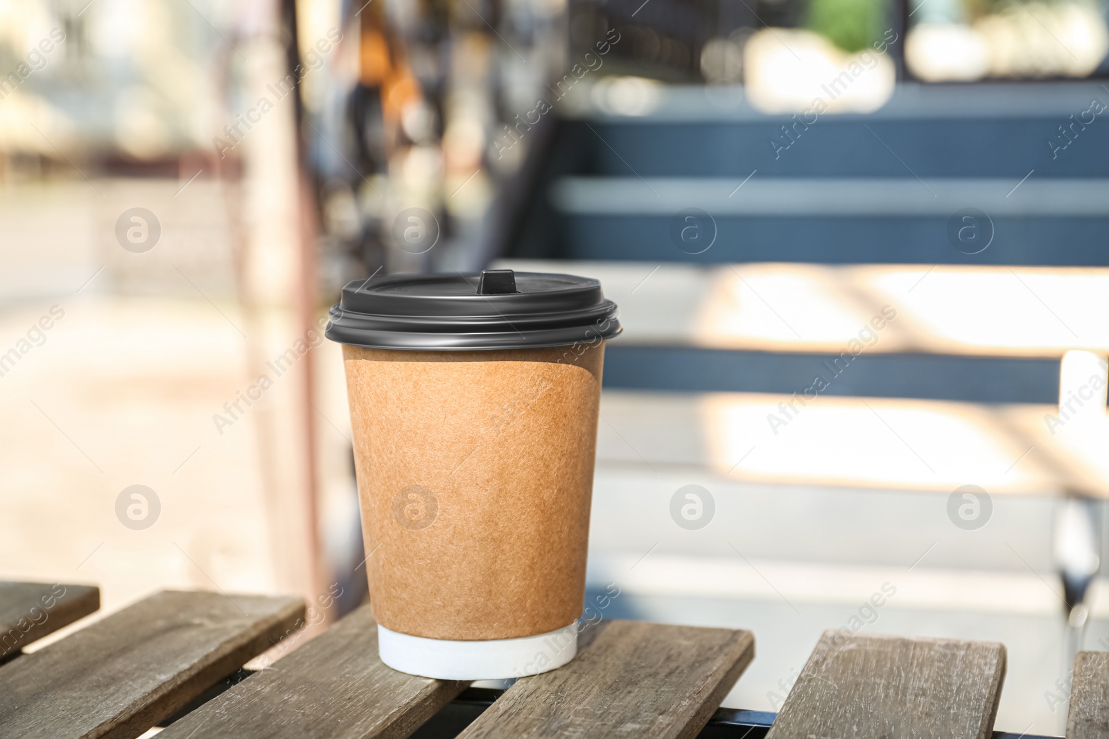 Photo of Paper cup on wooden bench outdoors. Takeaway drink