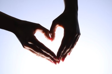 Woman making heart gesture on light background, closeup