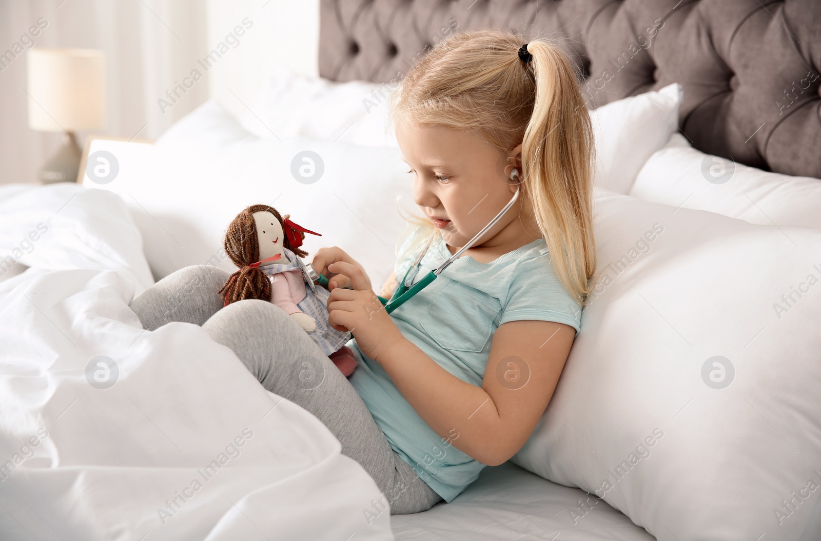 Photo of Cute child imagining herself as doctor while playing with stethoscope and doll at home