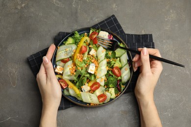 Photo of Woman eating delicious salad with lentils, vegetables and cheese at grey table, top view