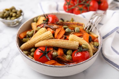 Tasty roasted baby corn with tomatoes and capers on white marble table, closeup