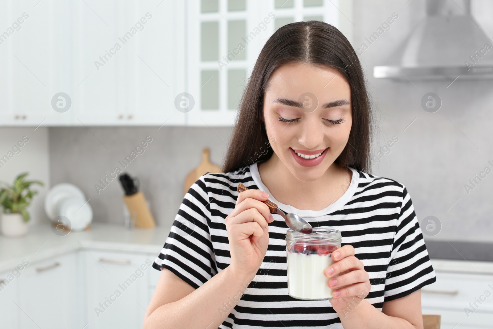 Photo of Happy woman with tasty yogurt in kitchen