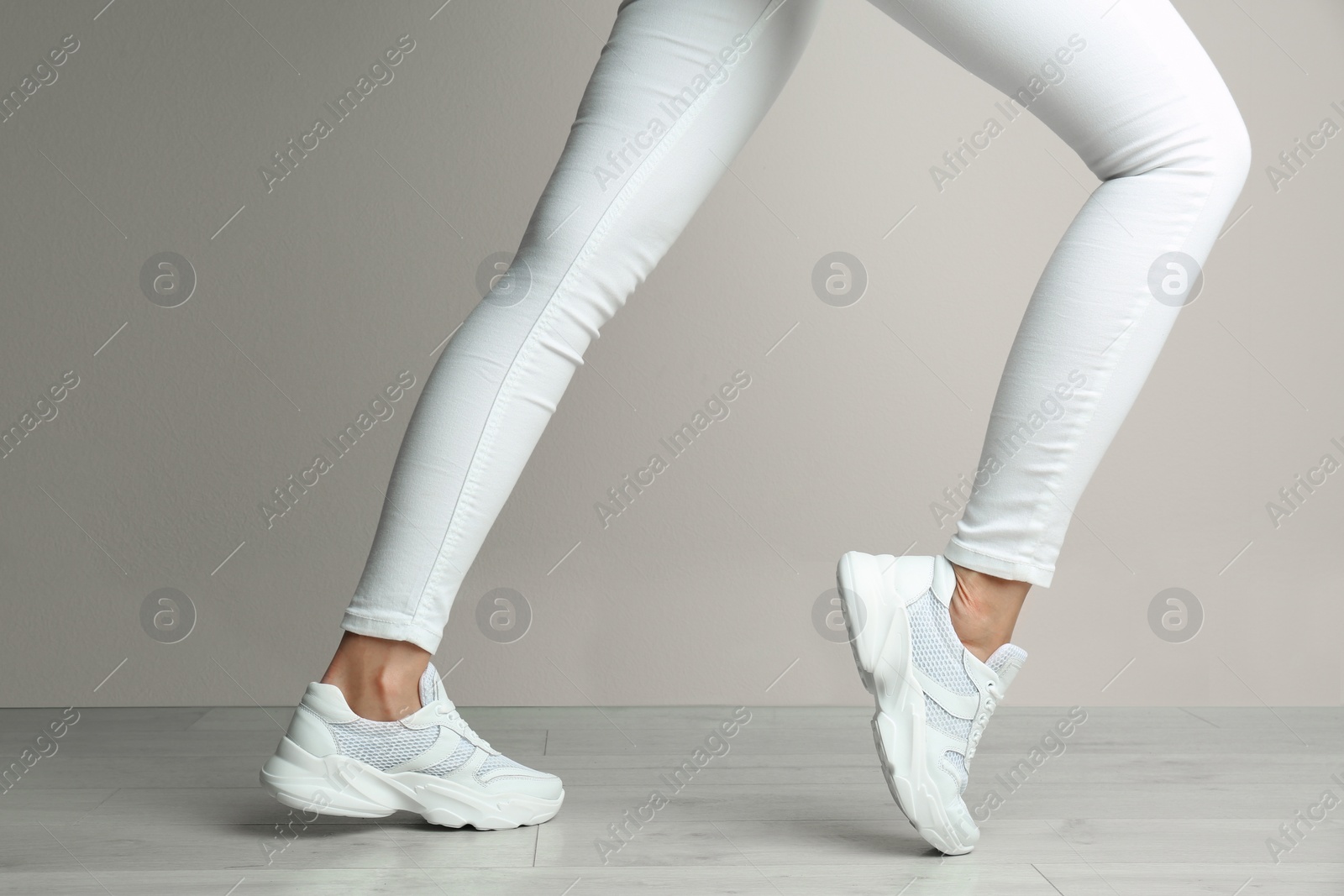 Photo of Woman wearing stylish sneakers near beige wall indoors, closeup