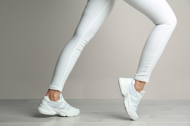 Woman wearing stylish sneakers near beige wall indoors, closeup