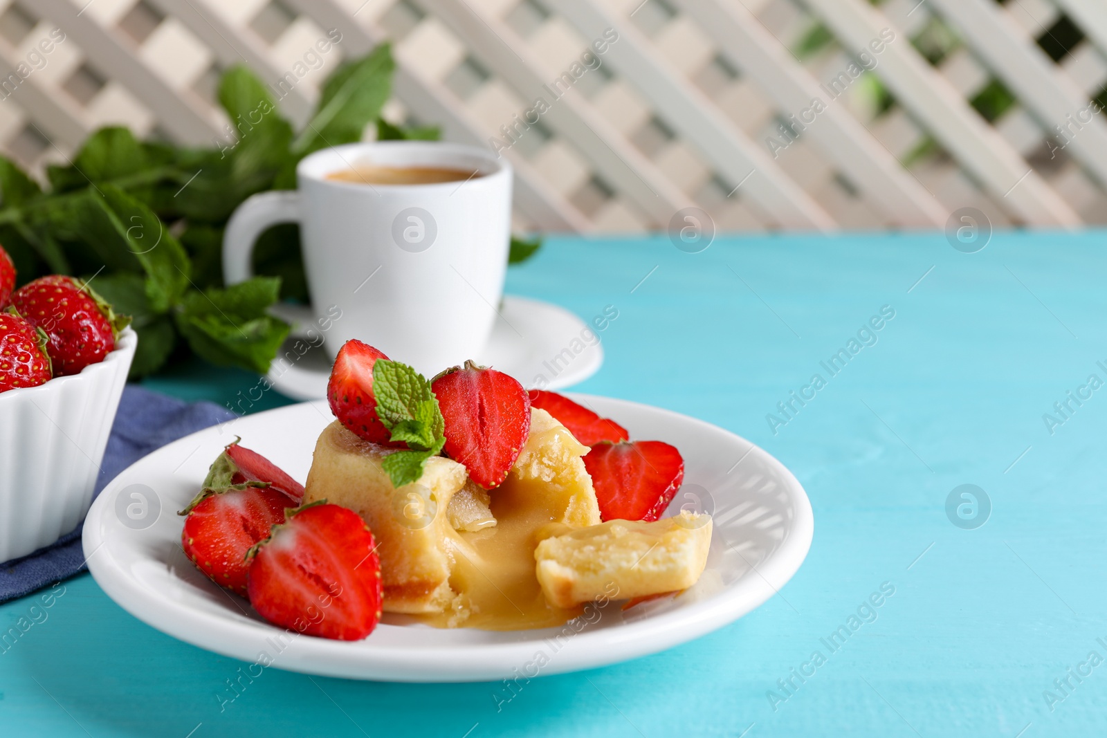 Photo of Tasty vanilla fondant with white chocolate and strawberries on light blue wooden table, space for text