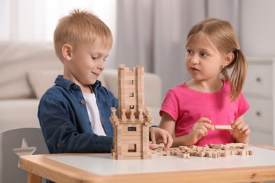 Photo of Little girl and boy playing with wooden tower at table indoors. Children's toy