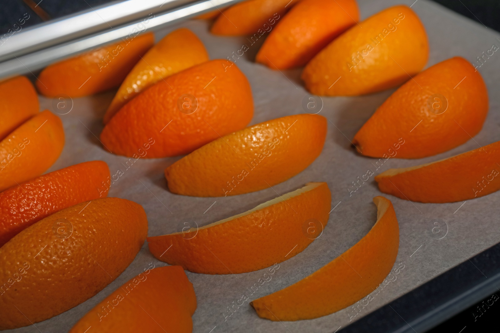Photo of Fresh orange peels on white parchment paper in oven, closeup