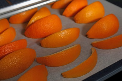 Fresh orange peels on white parchment paper in oven, closeup