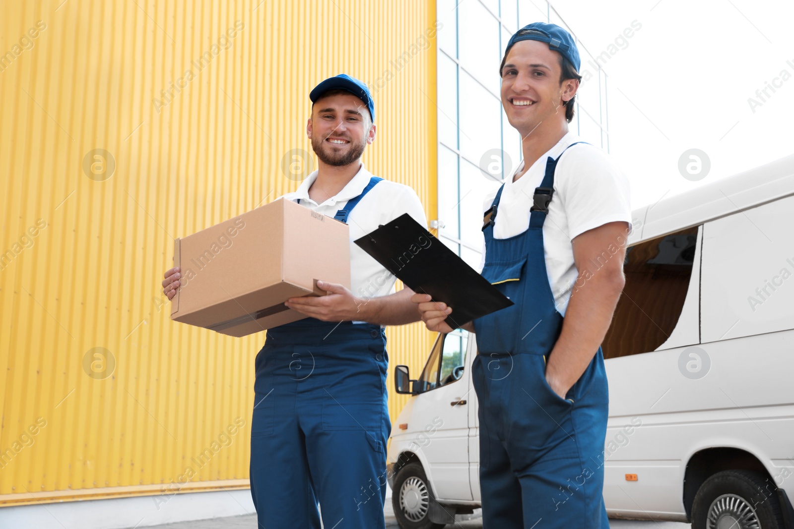 Photo of Male movers with box and clipboard near van outdoors