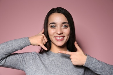 Woman showing CALL ME gesture in sign language on color background