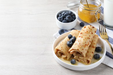 Photo of Delicious crepes served with blueberries, honey and milk on white wooden table. Space for text