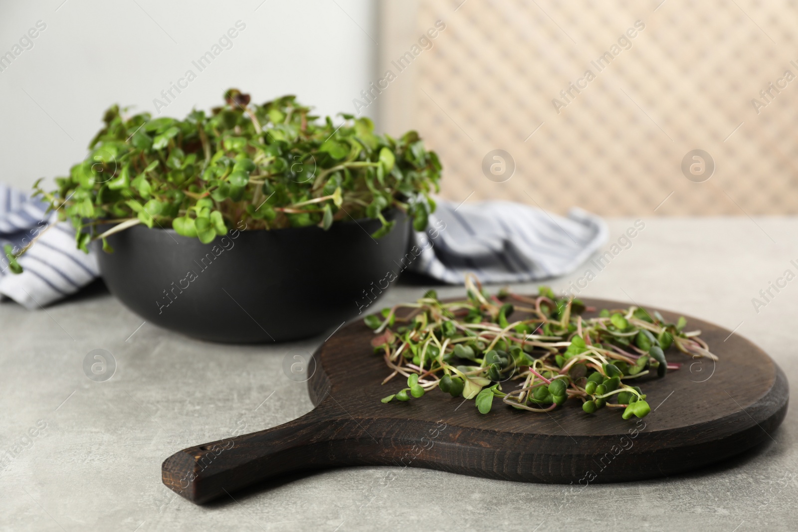 Photo of Board and bowl with fresh radish microgreens on light grey table
