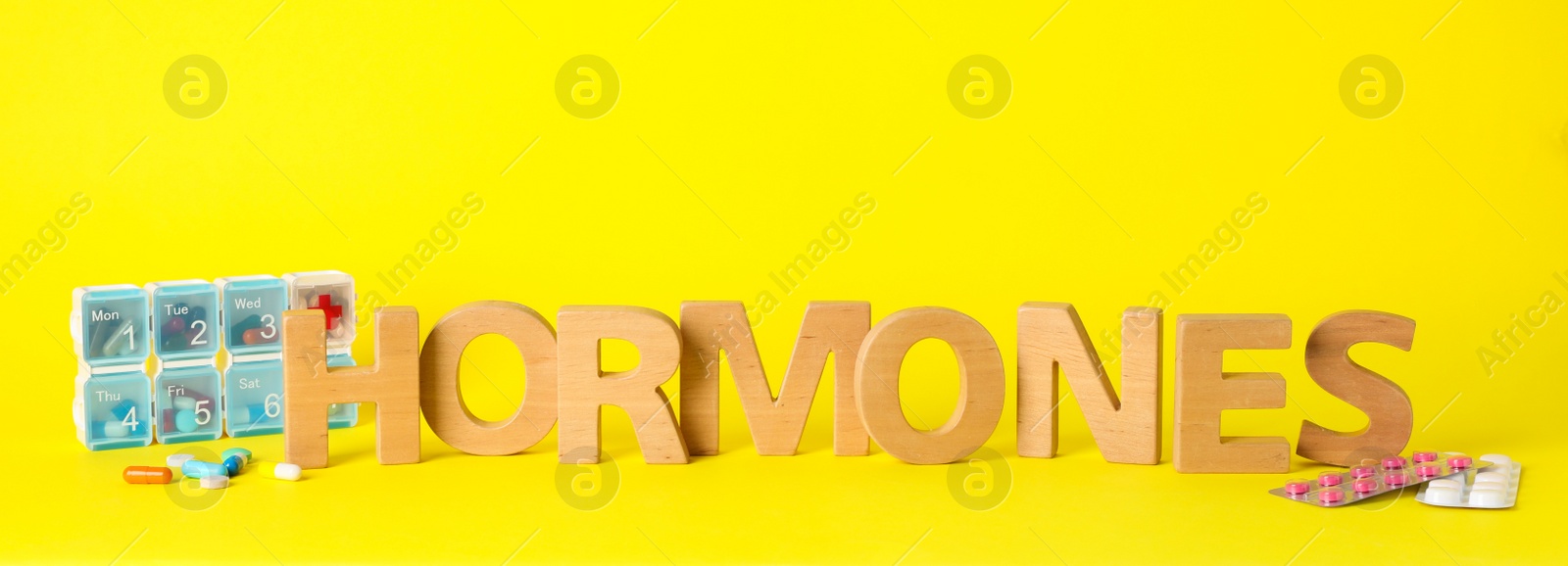 Photo of Word Hormones made of wooden letters and pills on yellow background