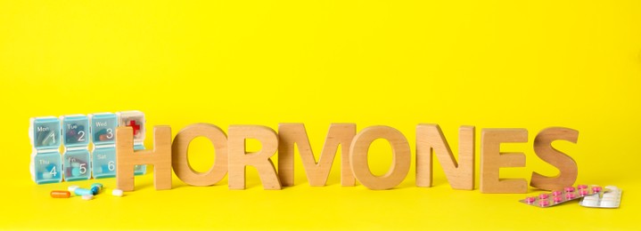 Word Hormones made of wooden letters and pills on yellow background