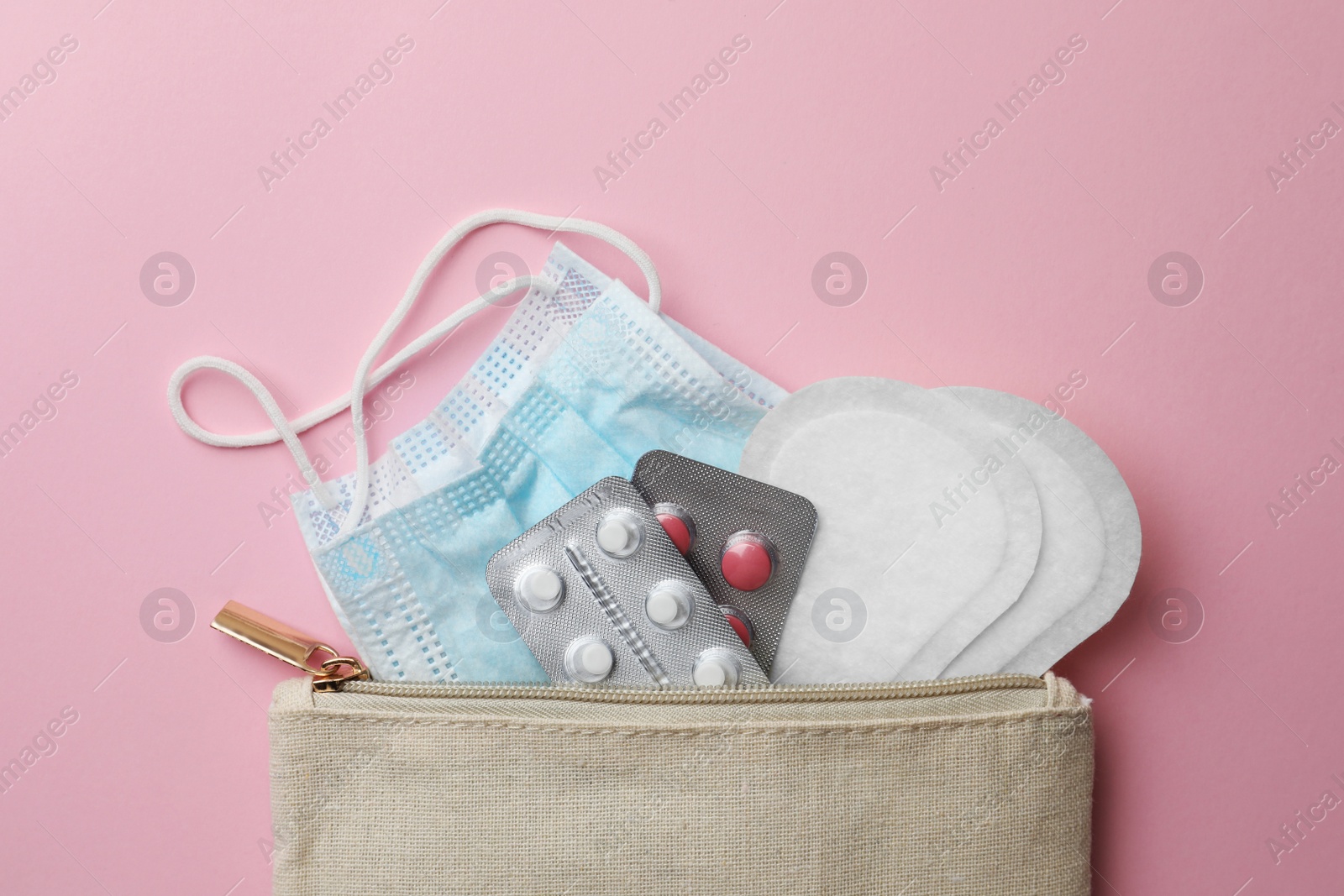 Photo of Bag with facial mask, pills and sanitary pads on pink background, top view