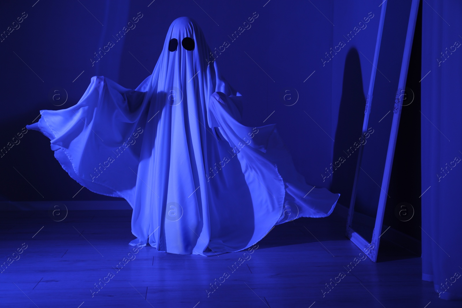 Photo of Creepy ghost. Woman covered with sheet in blue light