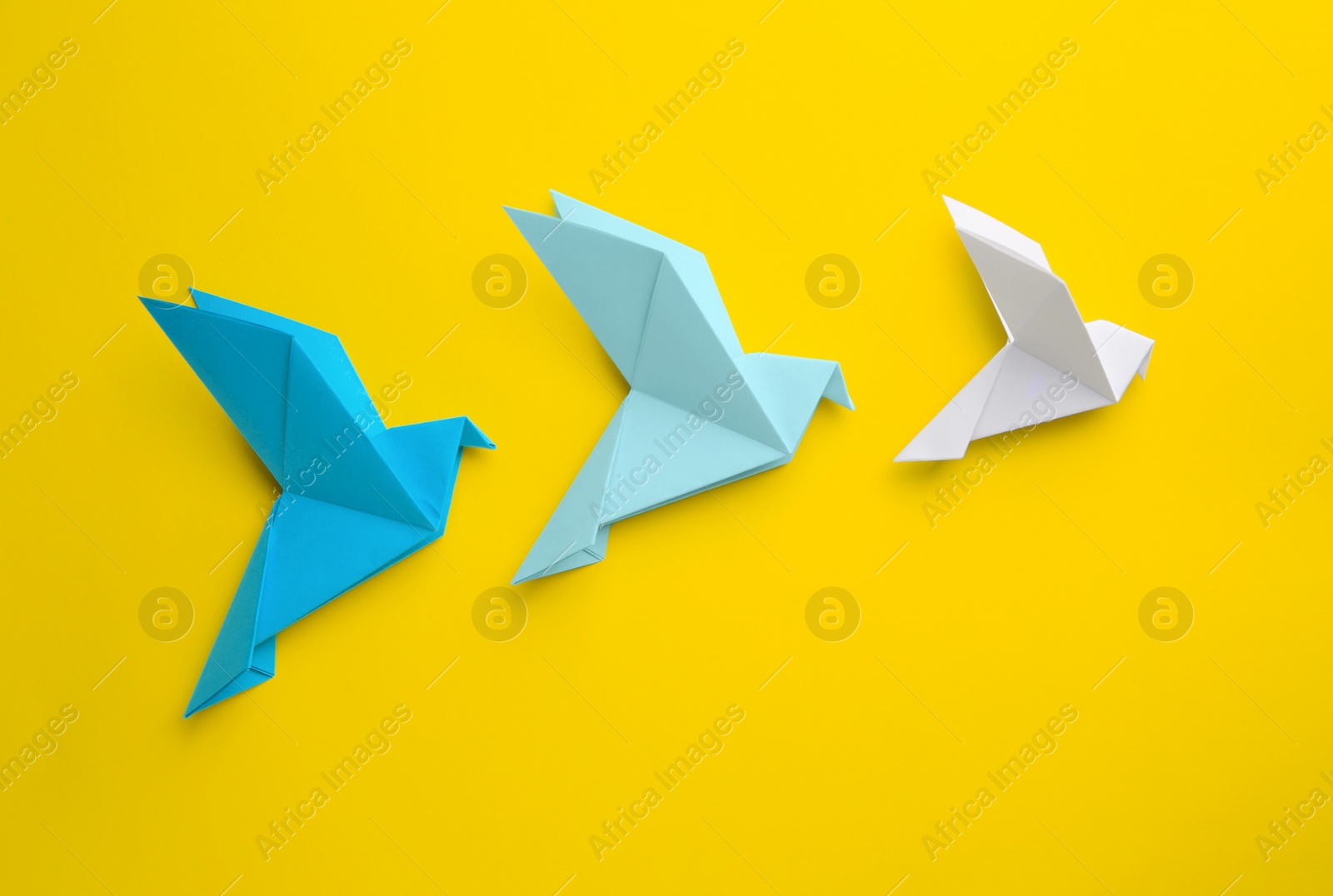 Photo of Origami art. Colorful handmade paper birds on yellow background, flat lay