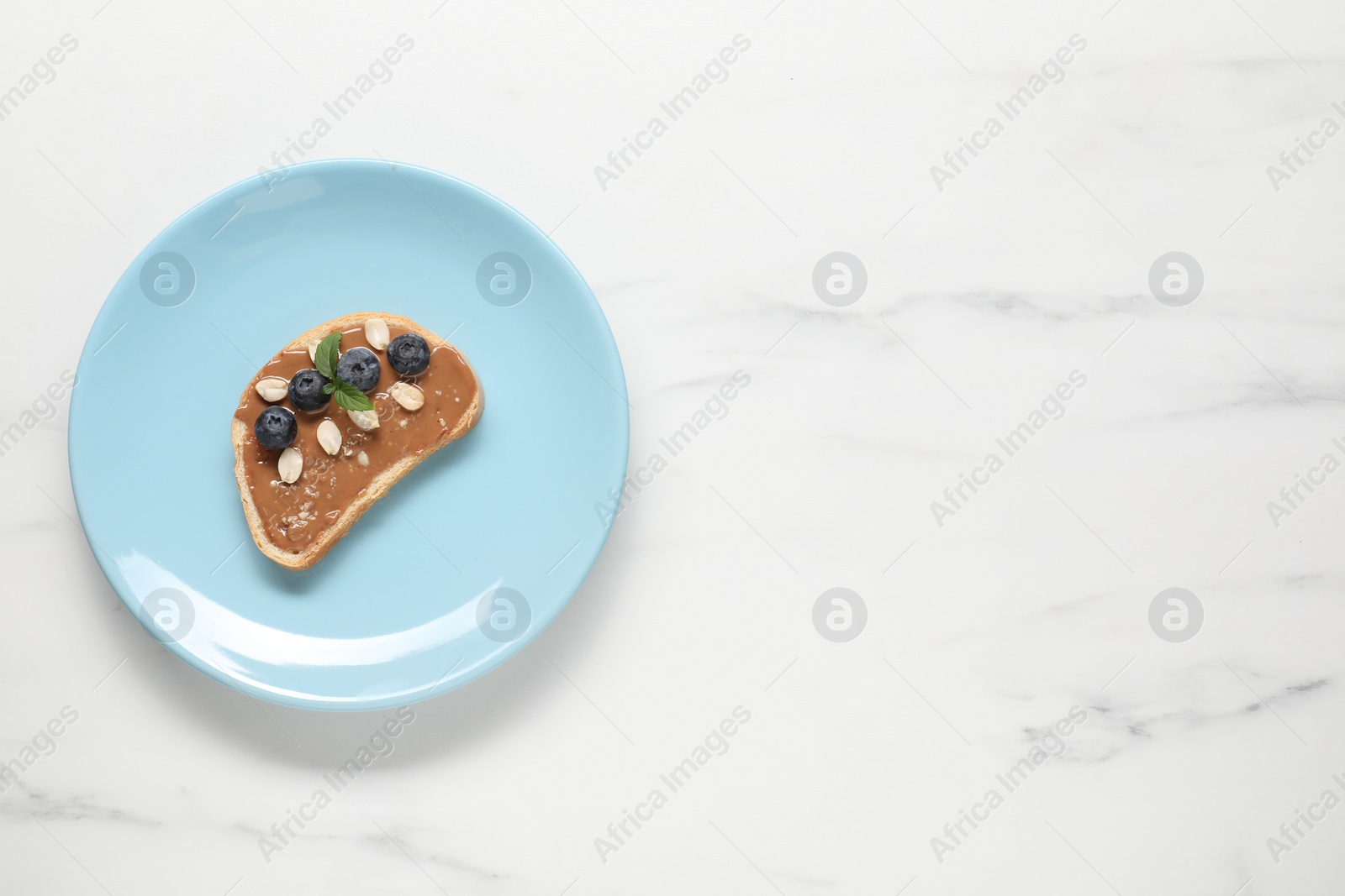 Photo of Toast with tasty nut butter, blueberries and peanuts on white marble table, top view. Space for text