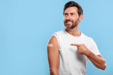Photo of Man pointing at sticking plaster after vaccination on his arm against light blue background