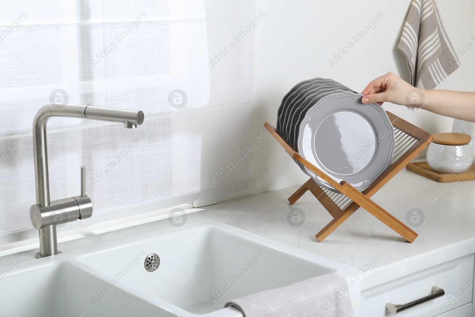 Photo of Woman taking grey plate from wooden holder in kitchen, closeup