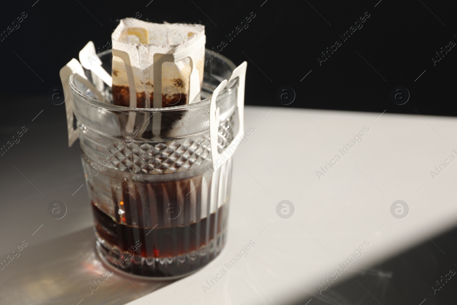 Photo of Glass with drip coffee bag on light grey table, closeup. Space for text
