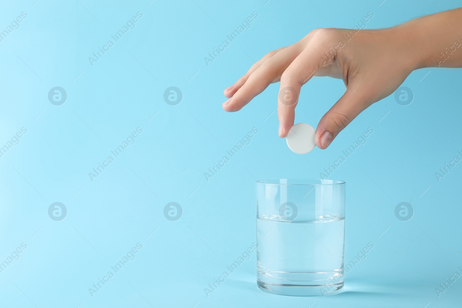 Photo of Woman putting tablet into glass of water on light blue background, space for text