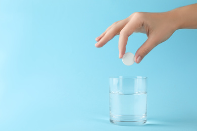 Photo of Woman putting tablet into glass of water on light blue background, space for text