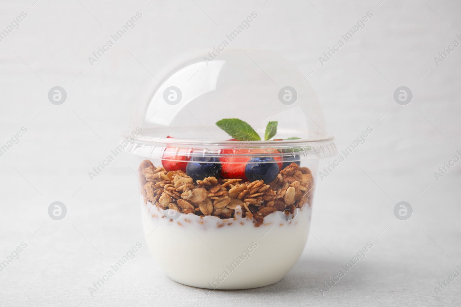 Photo of Tasty granola with berries and yogurt in plastic cup on light table