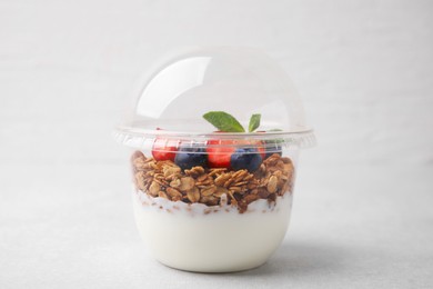 Photo of Tasty granola with berries and yogurt in plastic cup on light table