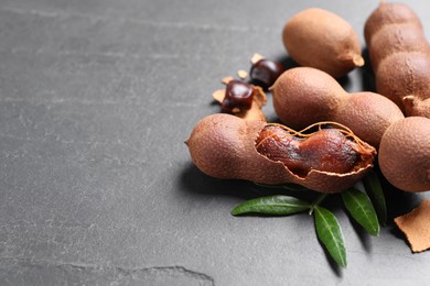 Delicious ripe tamarinds and leaves on black table. Space for text