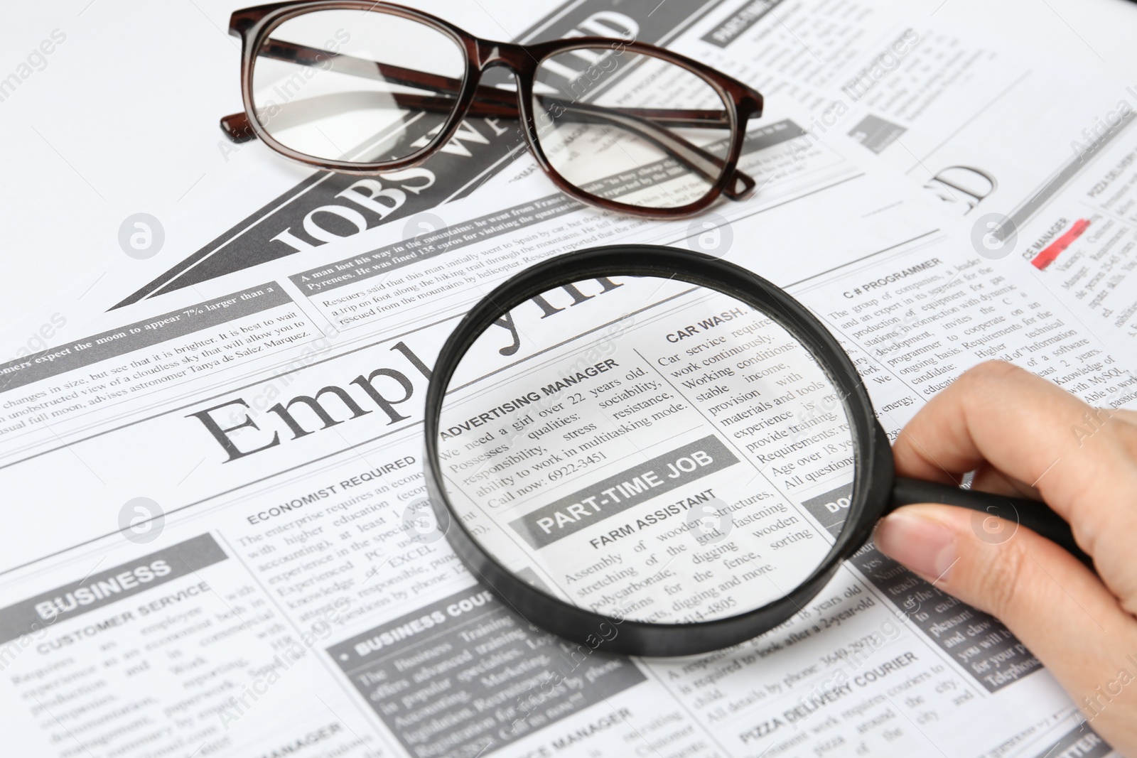 Photo of Woman looking through magnifying glass at newspaper, closeup. Job search concept