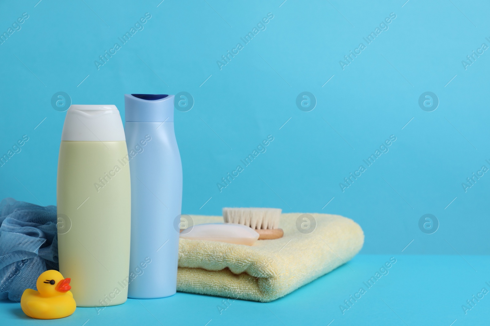 Photo of Baby cosmetic products, bath duck, accessories and towel on light blue background. Space for text