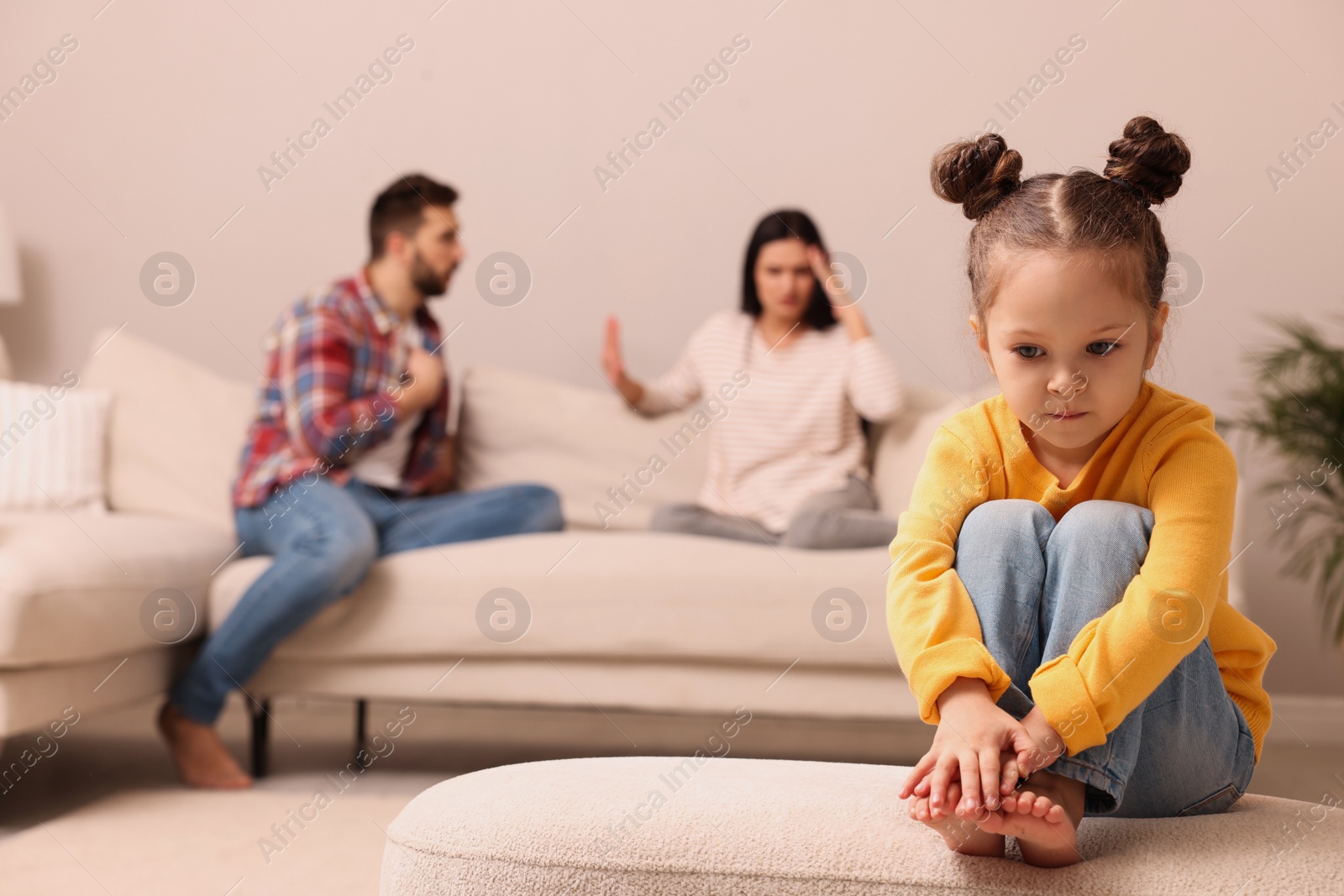 Photo of Sad little girl and her arguing parents on sofa in living room