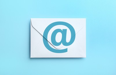 Image of White paper envelope with at sign on light blue background, top view. Email service