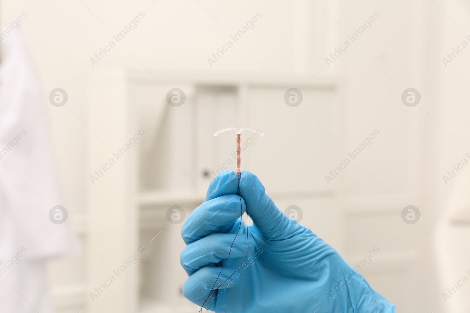 Photo of Doctor holding T-shaped intrauterine birth control device on blurred background, closeup