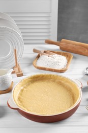 Photo of Pie tin with fresh dough, rolling pin and ingredients on white wooden table. Making quiche