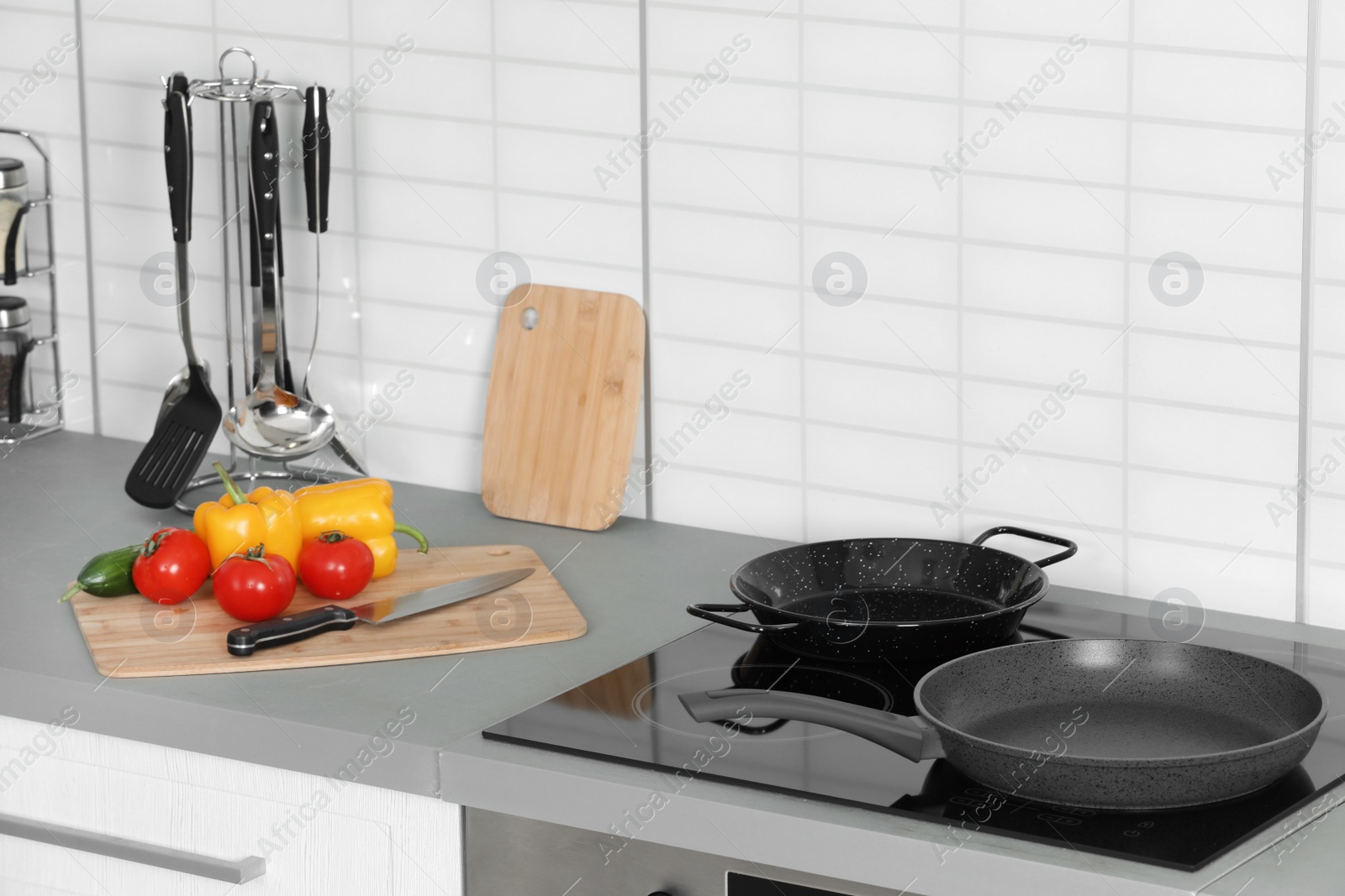 Photo of Clean frying pans and board with fresh vegetables in kitchen