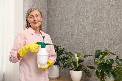 Photo of Happy housewife with plant mister near green houseplants at home