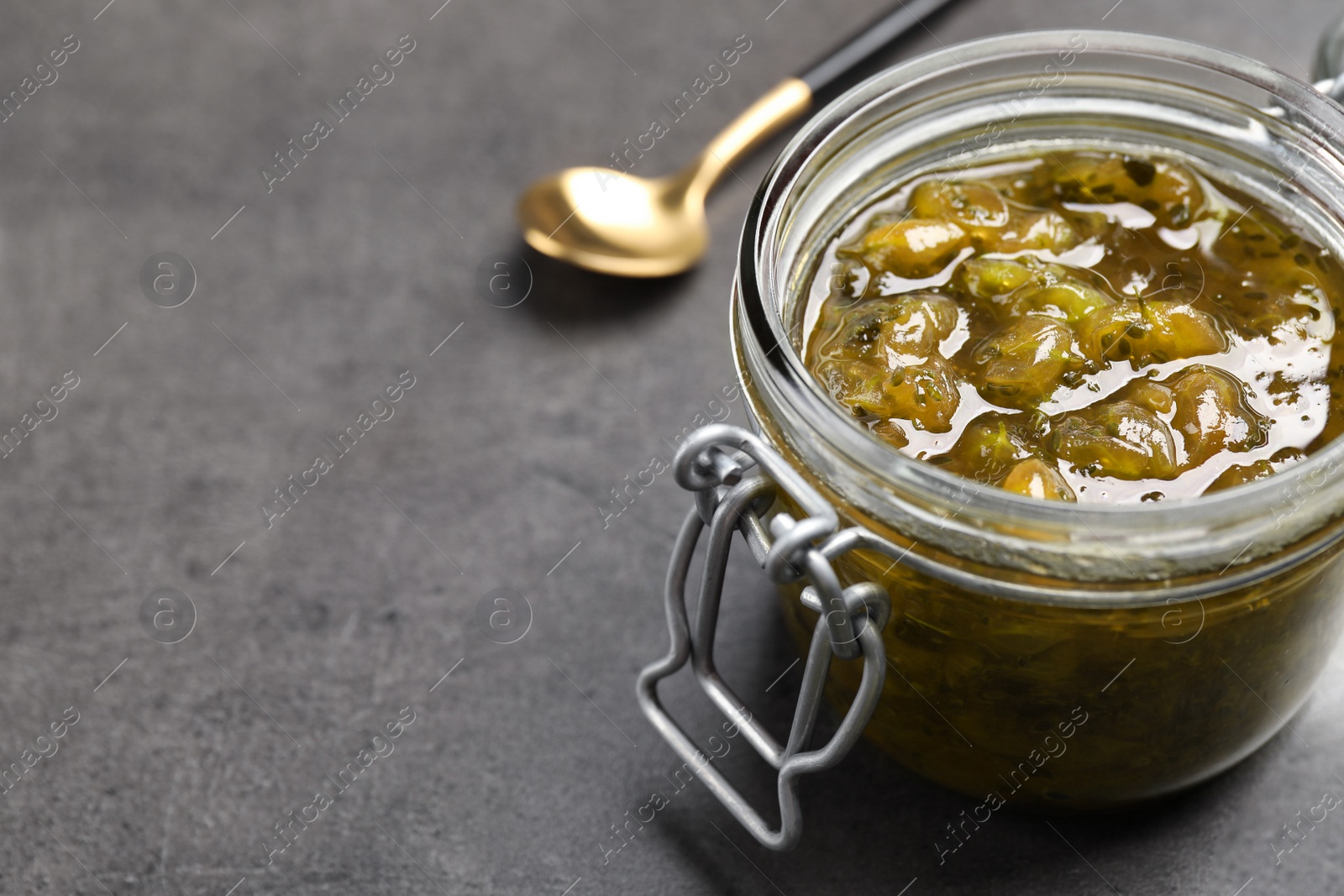 Photo of Jar of delicious gooseberry jam on grey table, closeup. Space for text