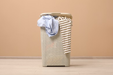 Photo of Plastic laundry basket with clothes near beige wall