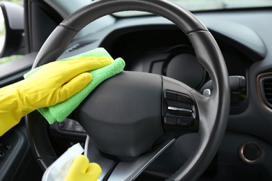 Photo of Woman cleaning steering wheel with rag in car, closeup