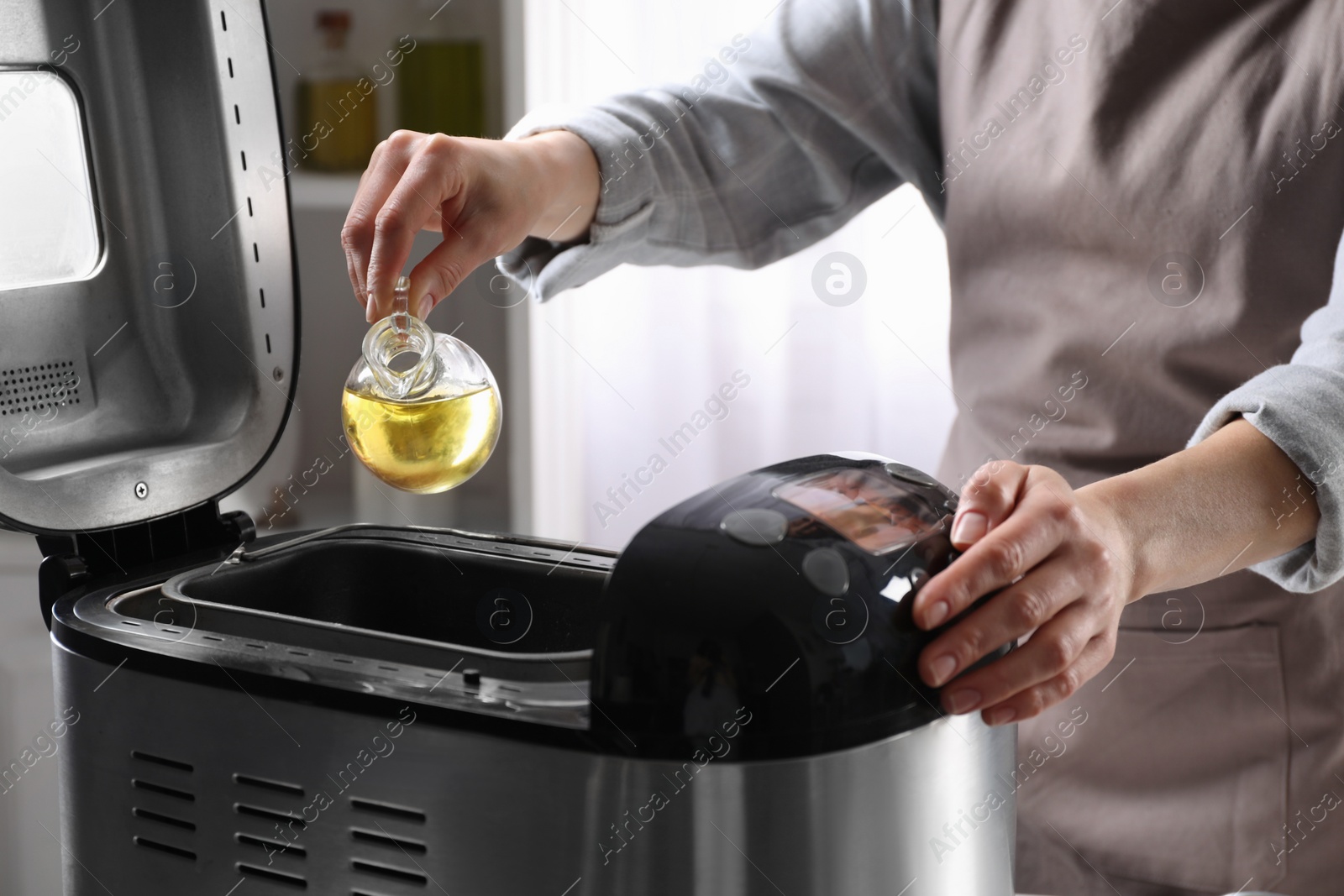 Photo of Woman pouring oil into breadmaker indoors, closeup