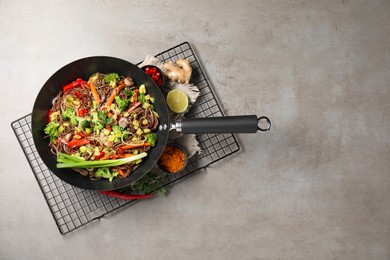 Photo of Stir-fry. Tasty noodles with meat in wok and ingredients on grey textured table, flat lay. Space for text