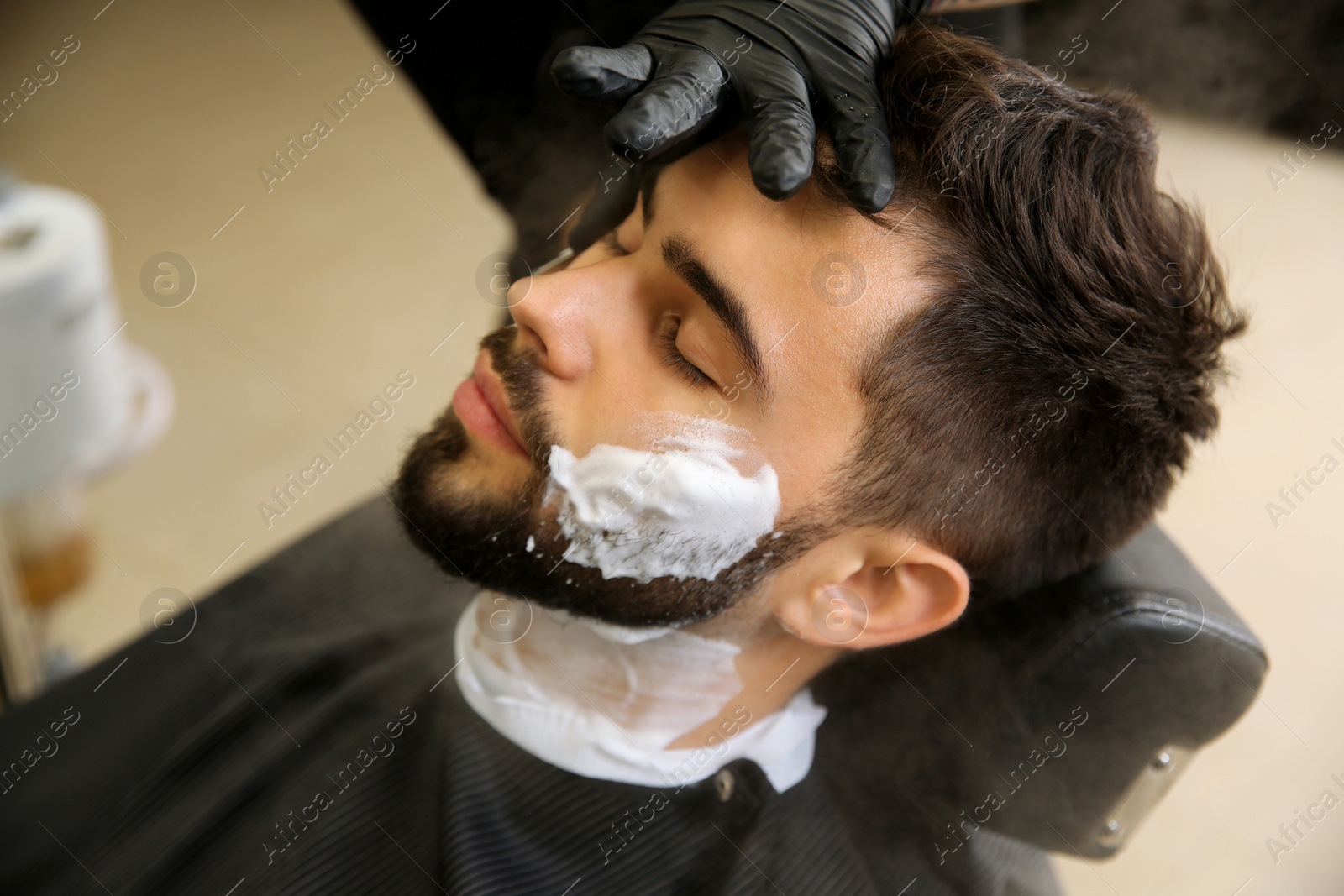 Photo of Young man visiting barbershop. Professional shaving service