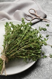 Photo of Bunch of aromatic thyme and scissors on grey table