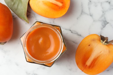 Delicious persimmon jam and fresh fruits on white marble table, flat lay