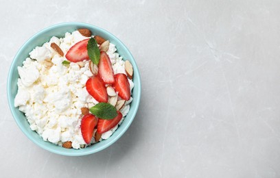 Fresh cottage cheese with strawberry and almond in bowl on light marble table, top view. Space for text
